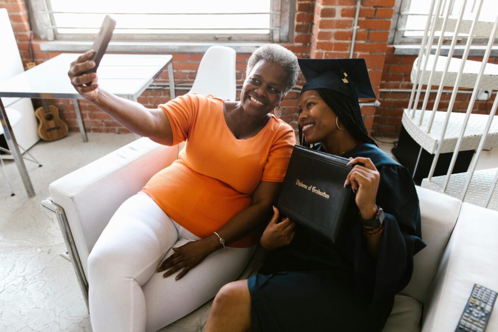 Two women celebrate together, with one wearing graduation cap while they take a happy selfie.