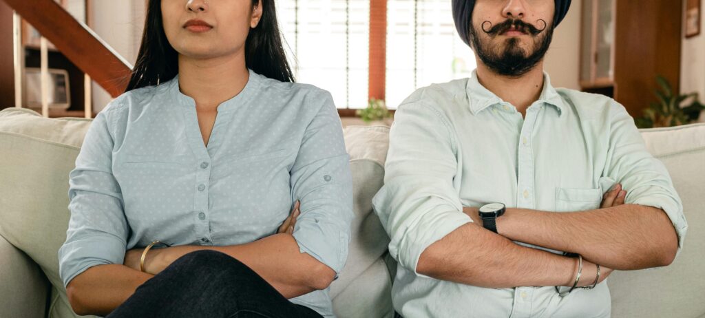 Couple sitting apart on couch with arms crossed, showing family relationship tension and signs of toxic dynamics that need addressing.