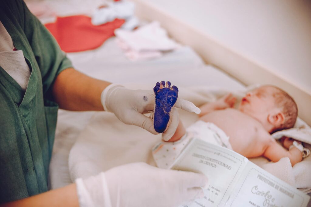 Medical professional in scrubs taking an ink footprint from a newborn baby's foot.