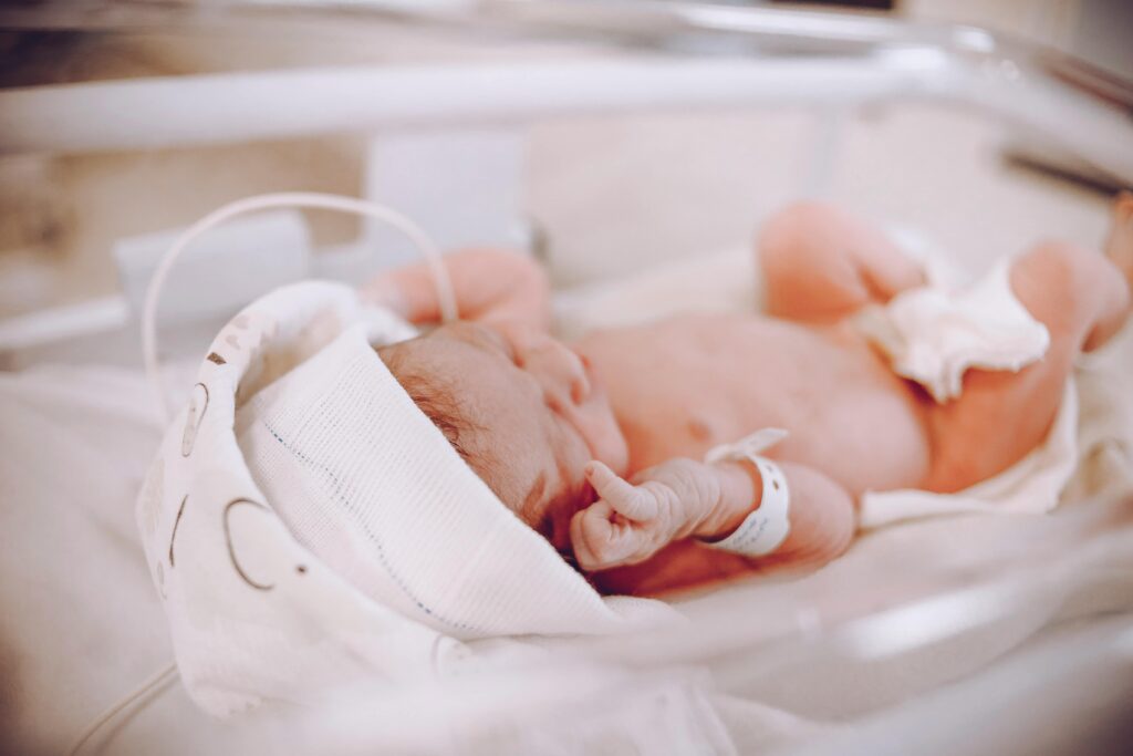 Newborn baby lying in clear hospital bassinet with medical monitoring equipment.