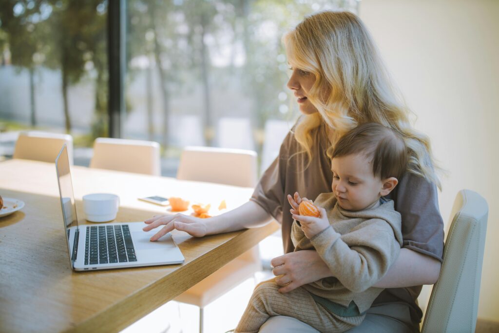 Woman Carrying her Baby and Working on a Laptop
