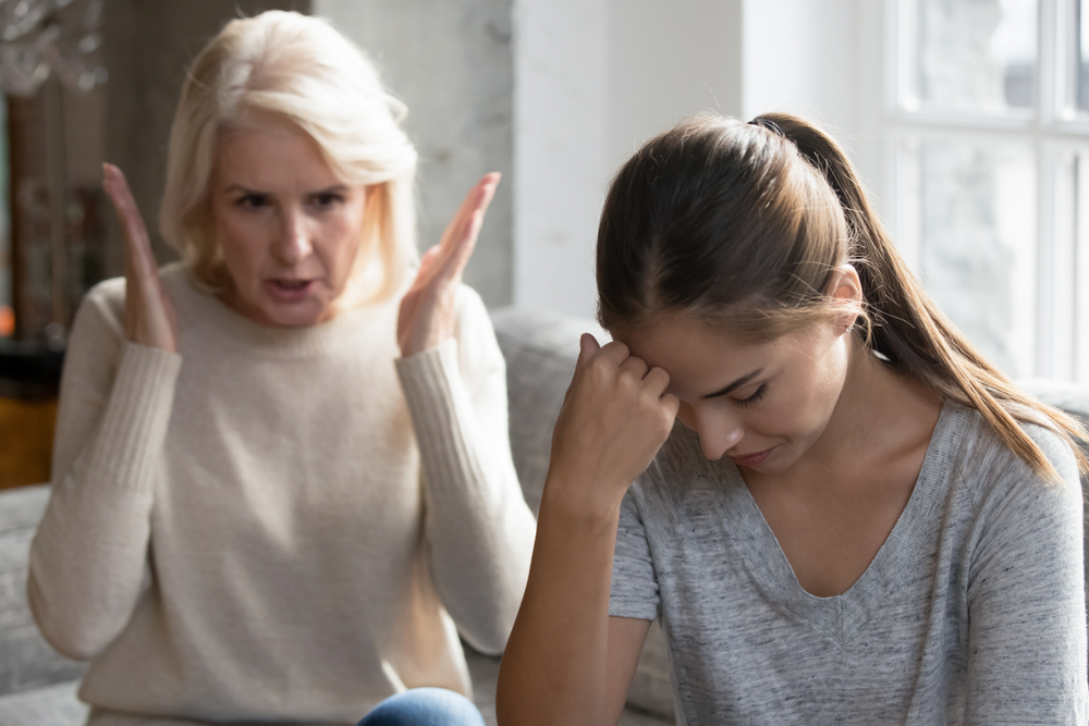 Mid aged mother sit on couch scold grown up daughter, angry mum tell complaints lecturing teen adult child feeling stressed, misunderstandings, generational gap, difficulties in relationships concept
