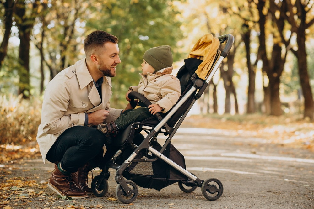 Father with little son walking in baby stroller in autumnal park
