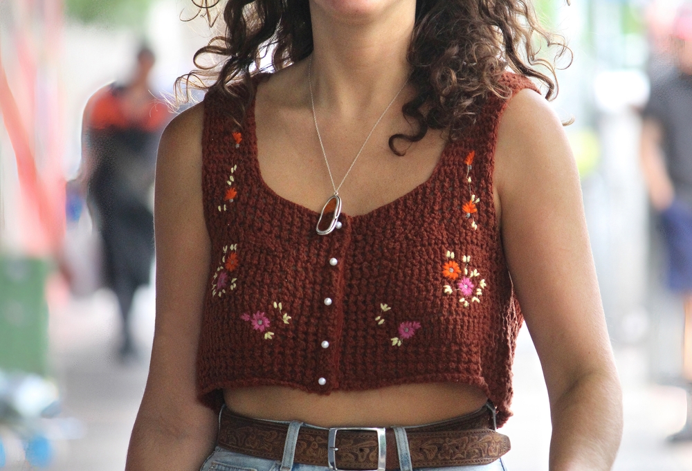 Young woman wearing a brown crochet crop top with flowers on it walking down the street