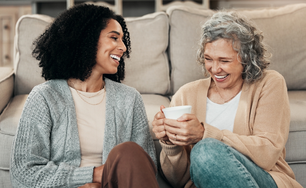 Love, mother and adult daughter on floor, coffee and conversation with happiness, break and laughing. Family, mama and female grown child on ground, tea and smile with rest, funny and quality time

