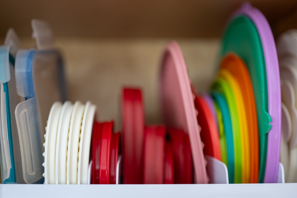 Narrow depth of field picture of an open kitchen cabinet with rows of organized storage of plastic lids.