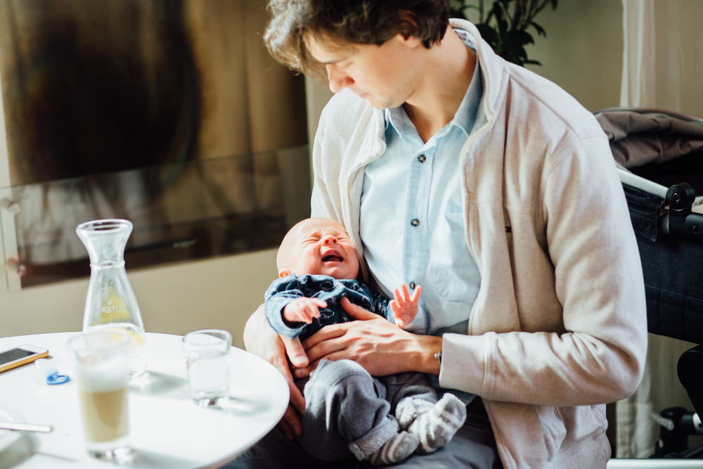 Newborn baby boy wake up and crying on the father's hands. Dad trying to calm his little son down while sitting in cafeteria or restaurant.
