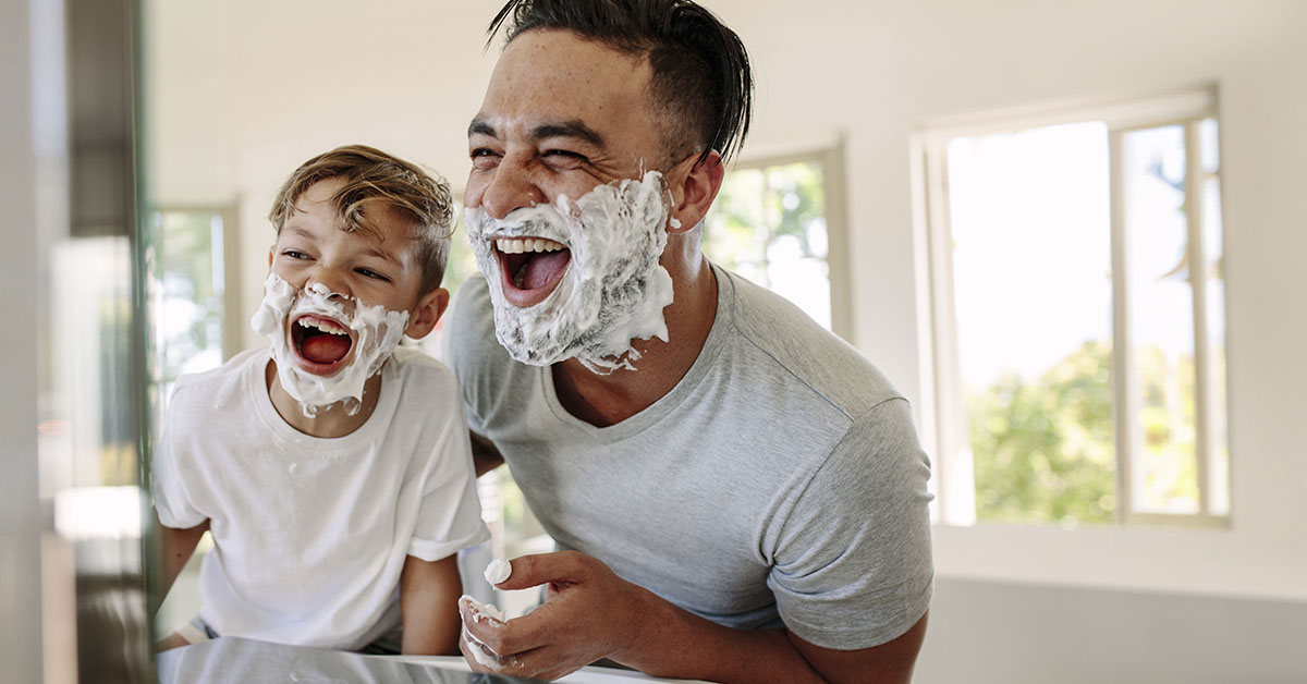father and young son laughing with shaving cream on their faces