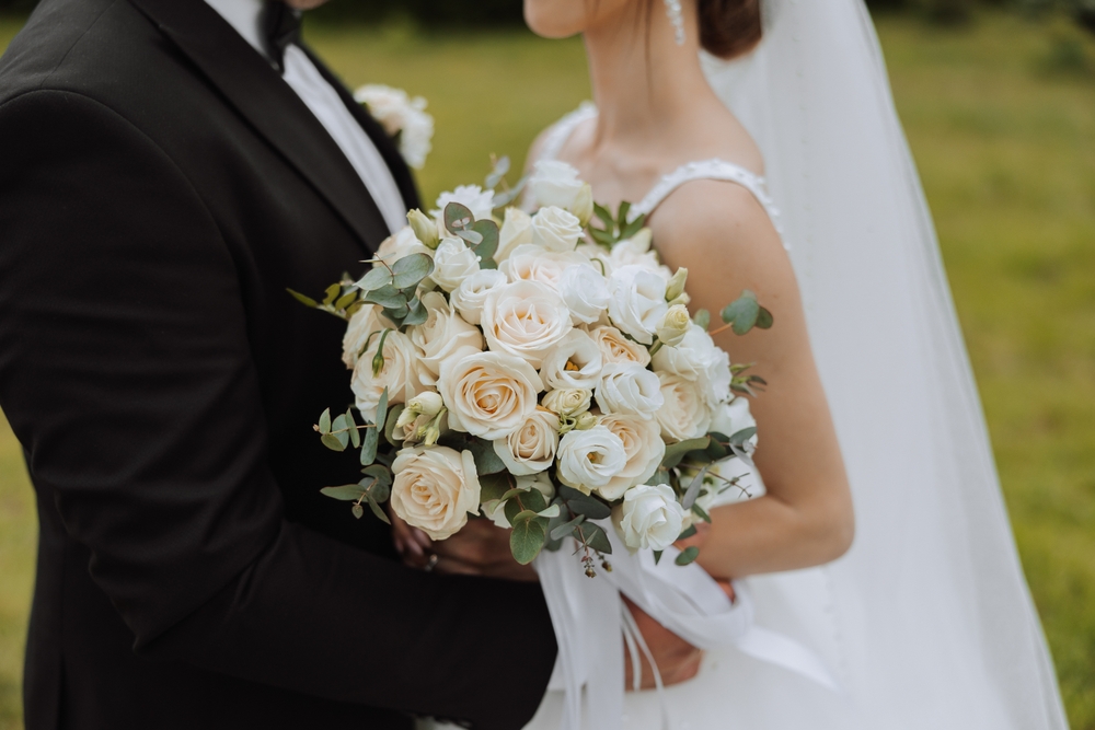 The groom hugs the bride from behind, the bride holds a wedding bouquet. Cropped photo. Groom in a black suit. Details