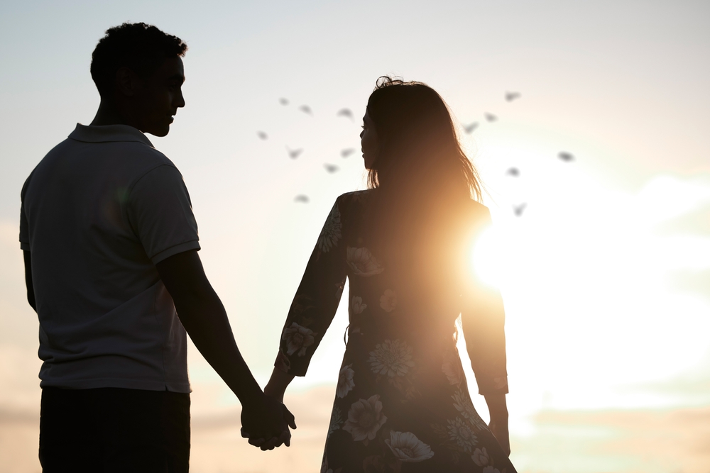 Couple, silhouette and holding hands at romantic, destination, holiday or honeymoon in summer at sunset on vacation on date. Woman, man and relationship in love or together, memory and travel on trip