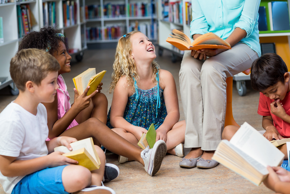 Low section of female teacher with smiling children reading books in library