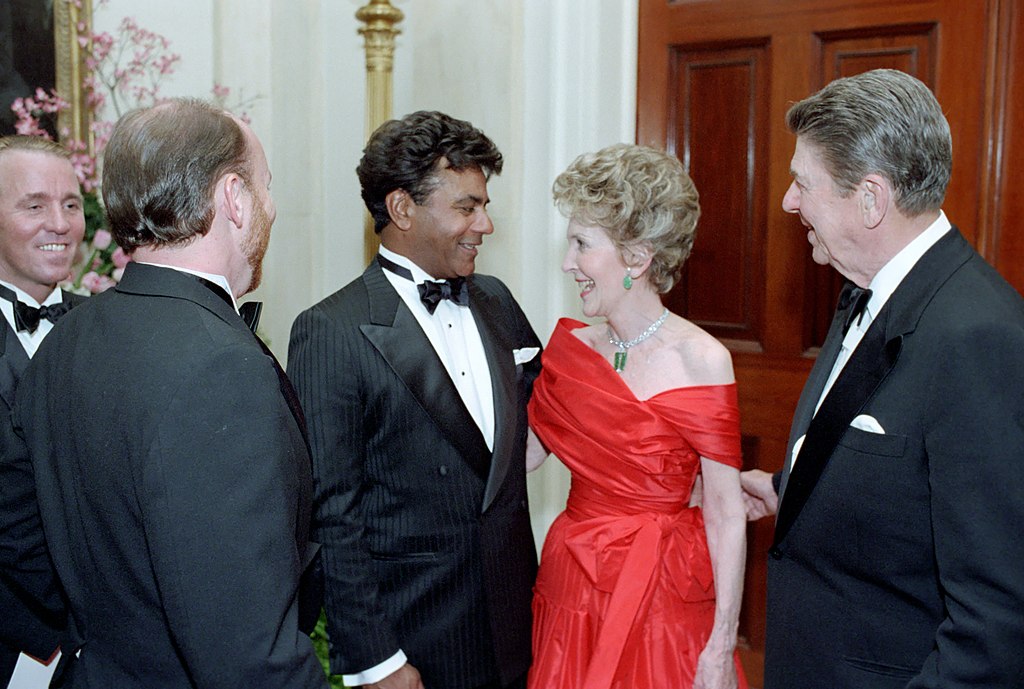 Johnny Mathis in a tuxedo speaking with President Ronald Reagan and First Lady Nancy Reagan in formal attire at a White House state dinner.