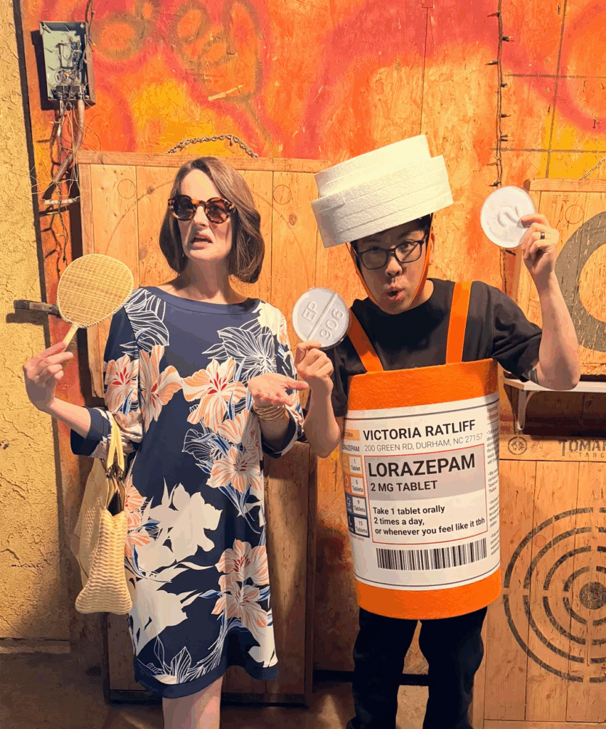 Woman wearing dress holding fan with man dressed as bottle of medication