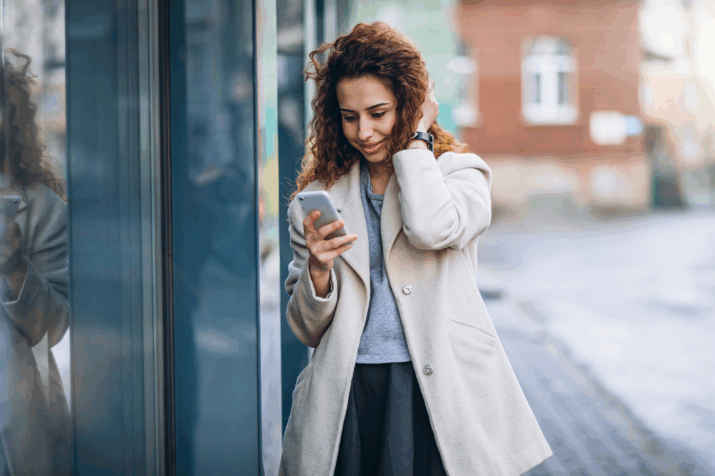 Young woman with curly hair using phone at the street