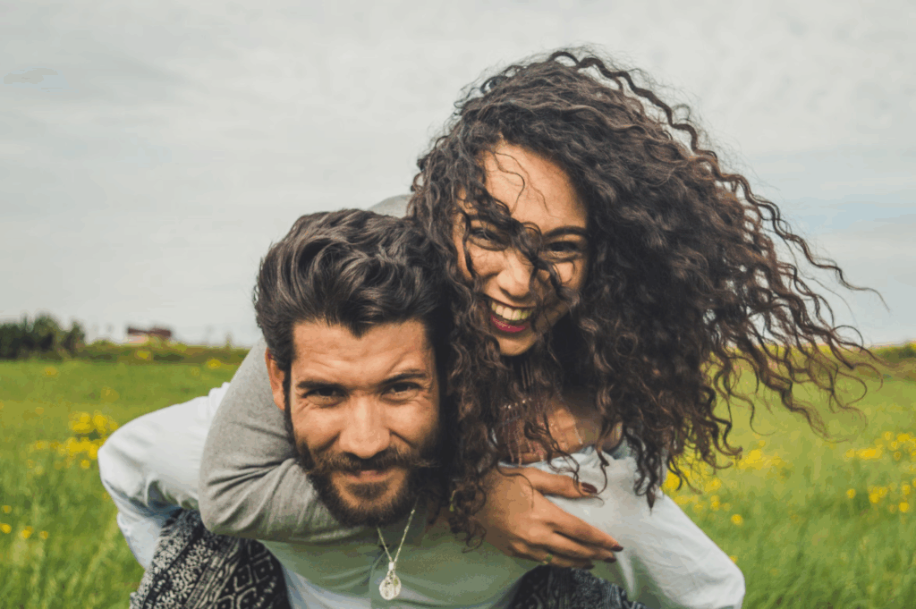 woman with curly hair with man wearing necklace in grass field