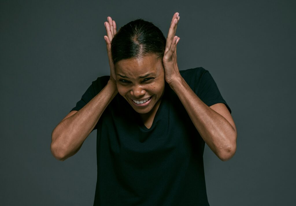 Person in dark clothing with hands pressed to their ears in distress.