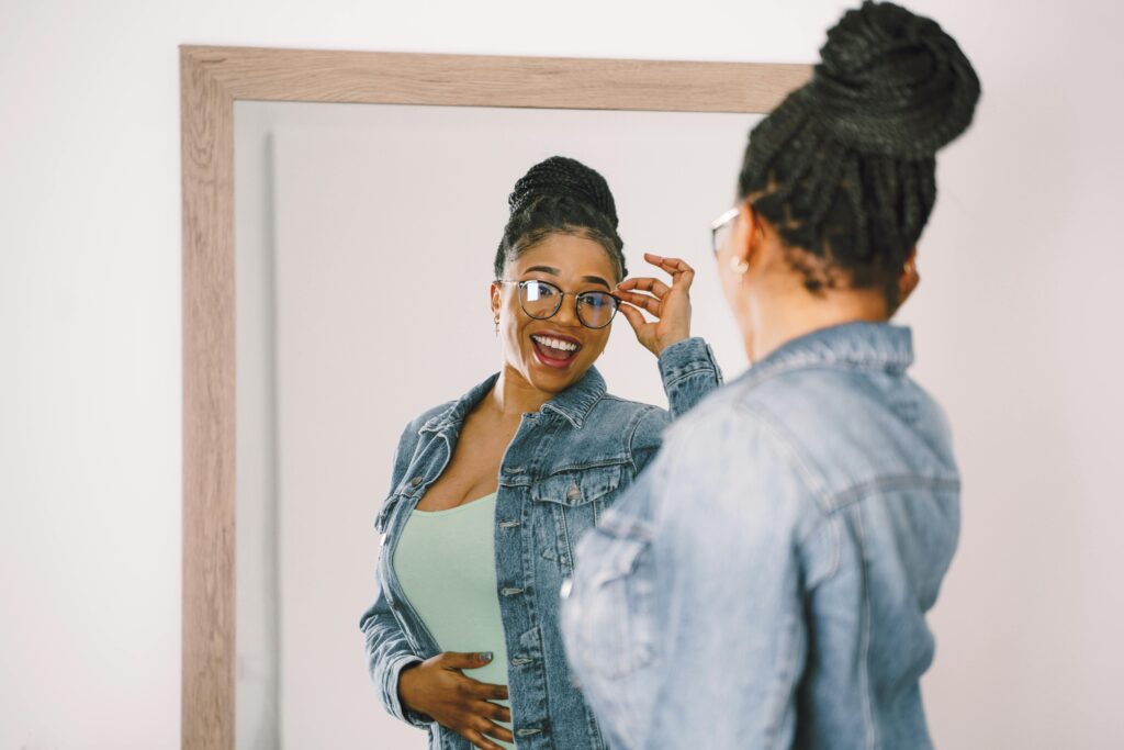 Woman smiling at her reflection while adjusting glasses.