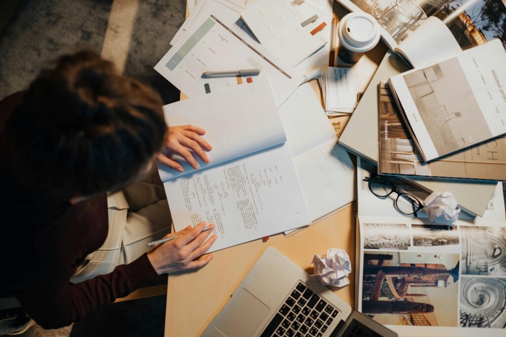 Overhead view of person working at a desk covered with papers and books.