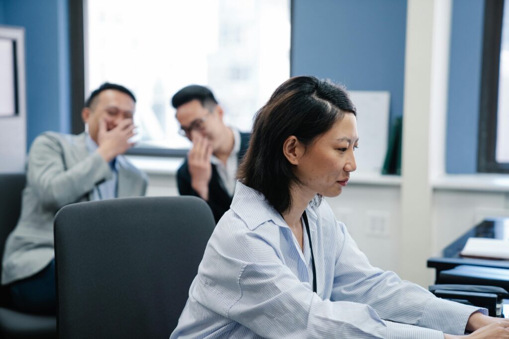 Woman at a desk looking down with two colleagues talking in the background.