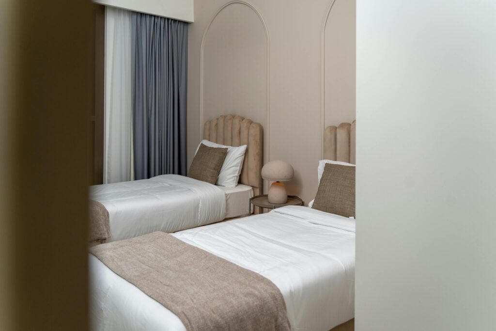 Two single beds side by side in a bedroom with matching beige headboards and white bedding.