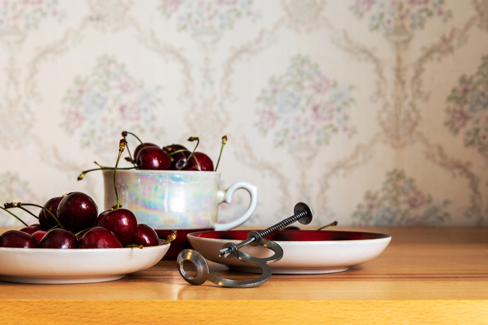 Vintage Cherry Pitter and sweet cherry in cup and saucer on a wooden desk in the retro interior.