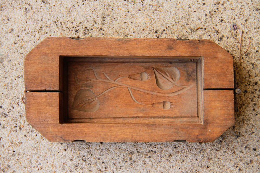 An antique object: an old wooden butter mold, articulated, placed on a light colored stone.