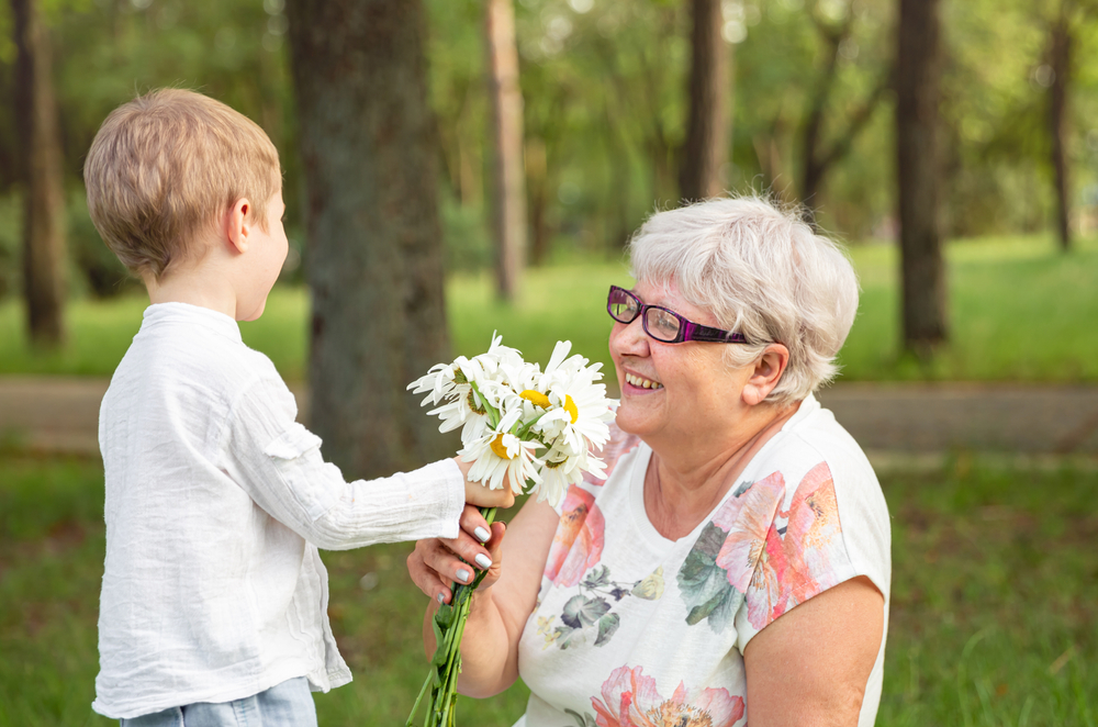 Beautiful boy giving a flower to grandma. Happy mothers day. Grandson and grandmother spending time together. Act of kindness to an elderly woman. Funny boy with flowers and his grandmother in park.