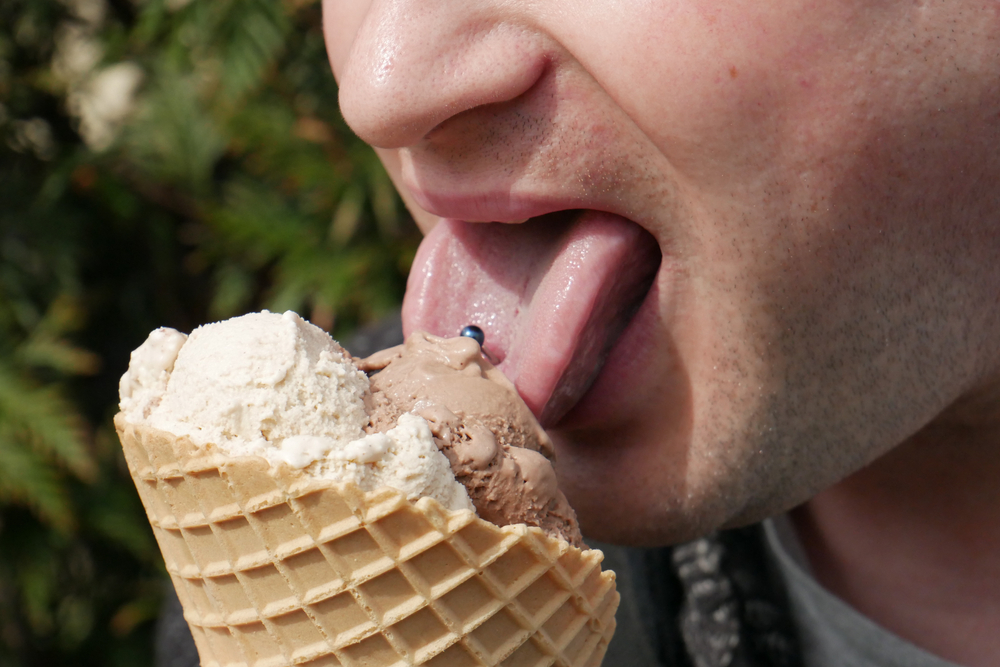 a man with a pierced tongue eats an ice cream in the sunshine