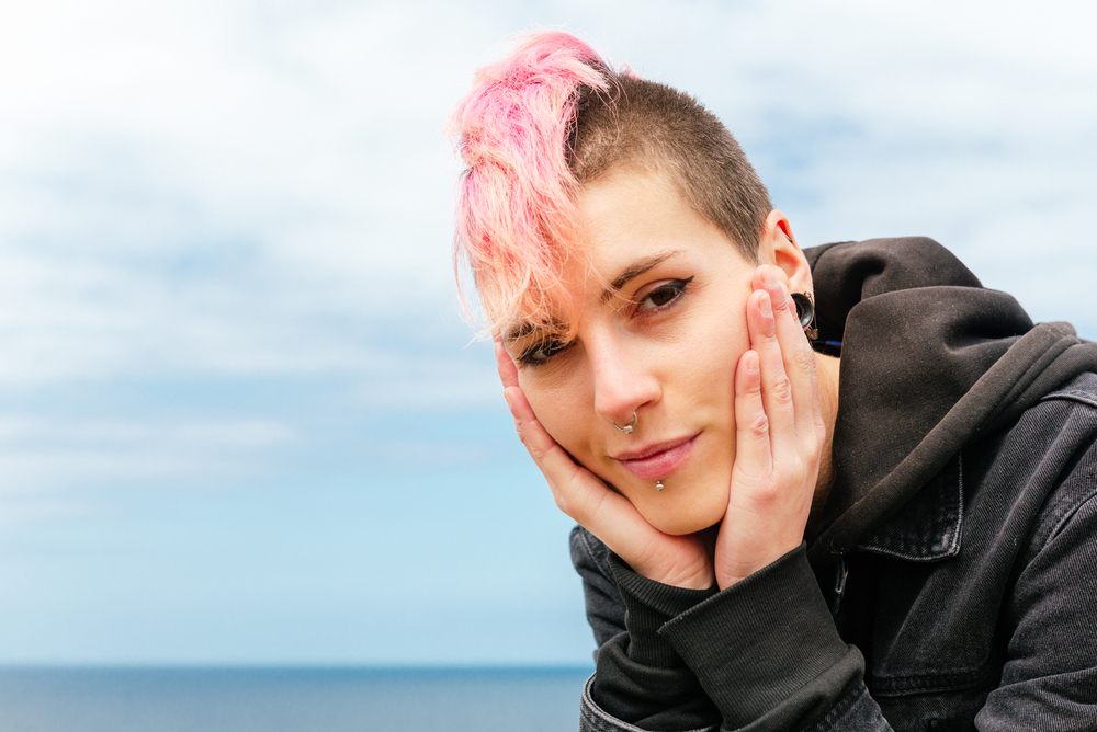 portrait of punk girl with pink hair looking at camera sweetly. Happy and serene woman with her hands on her face and with the sea in the background. urban tribes and youth