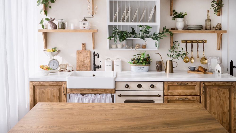 wooden tabletop with empty space on kitchen background. cozy interior with home decor, kitchenware, utensils, plates on shelf and green plants