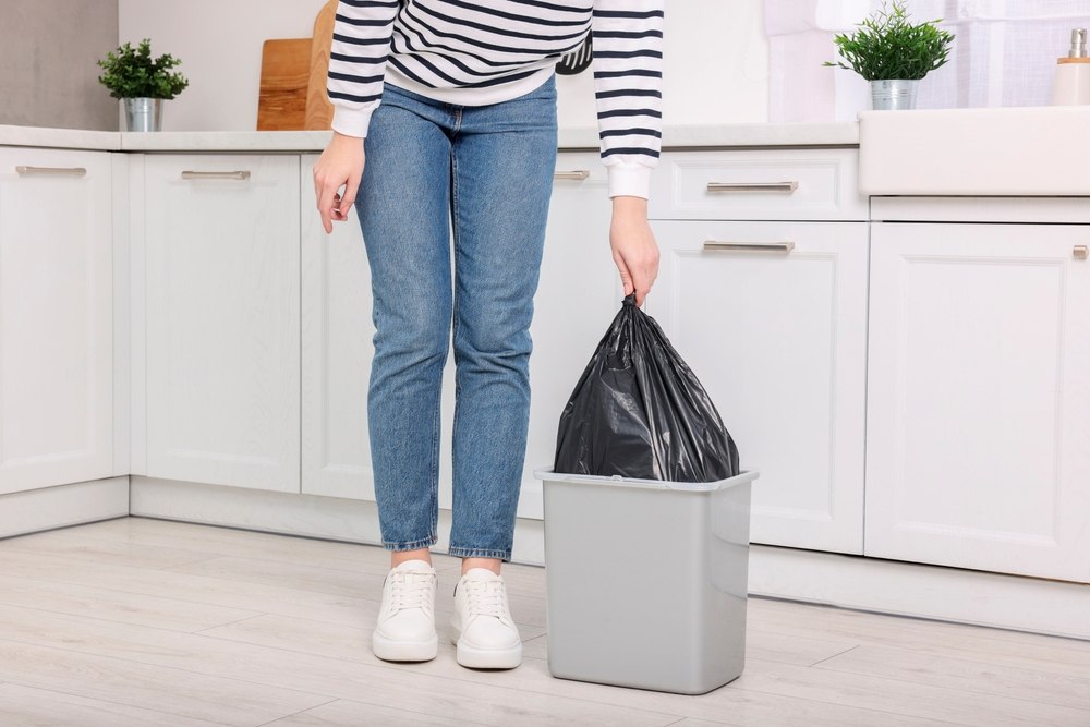 Woman taking garbage bag out of trash bin in kitchen, closeup