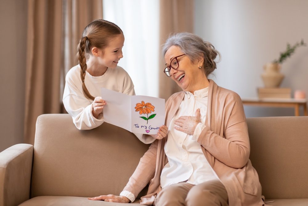 An older woman and a young girl are seated on a couch. The woman appears to be engaged in conversation with the girl, who is listening attentively