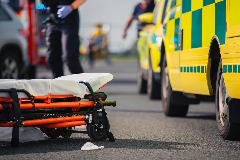 Selective focus on stretcher against ambulance cars of emergency medical service, firefighters and rescue helicopter on road. Themes rescue, urgency and health care.	
