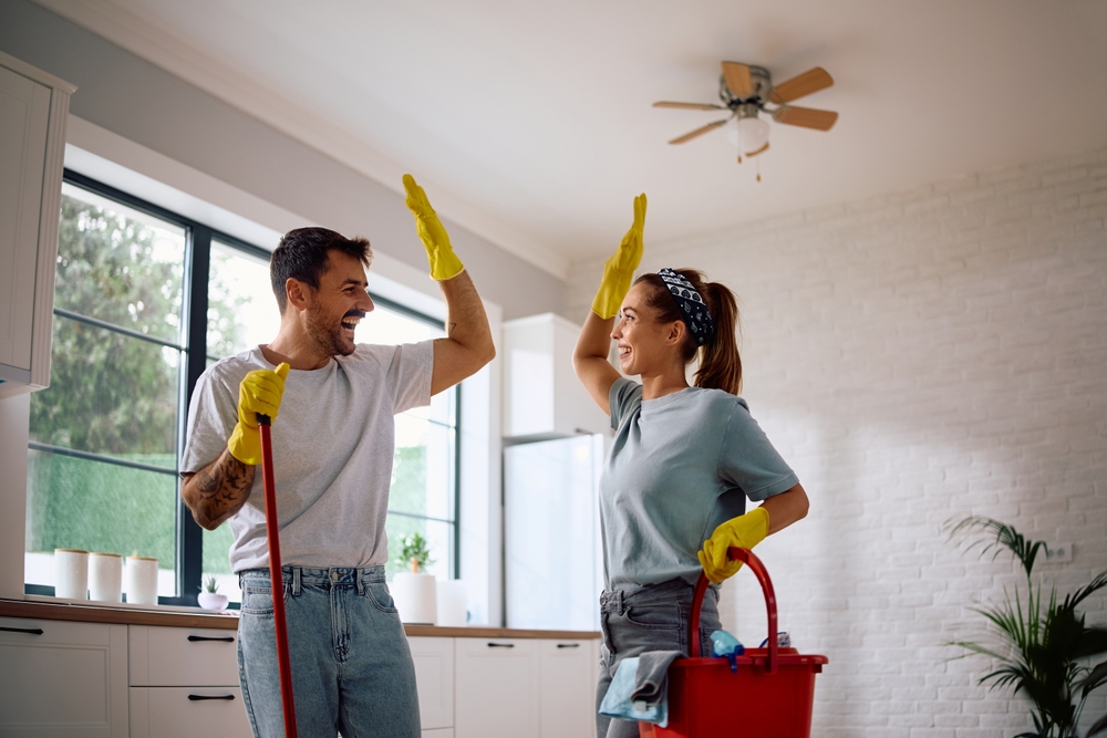 Happy couple giving high-five while cleaning their house together.