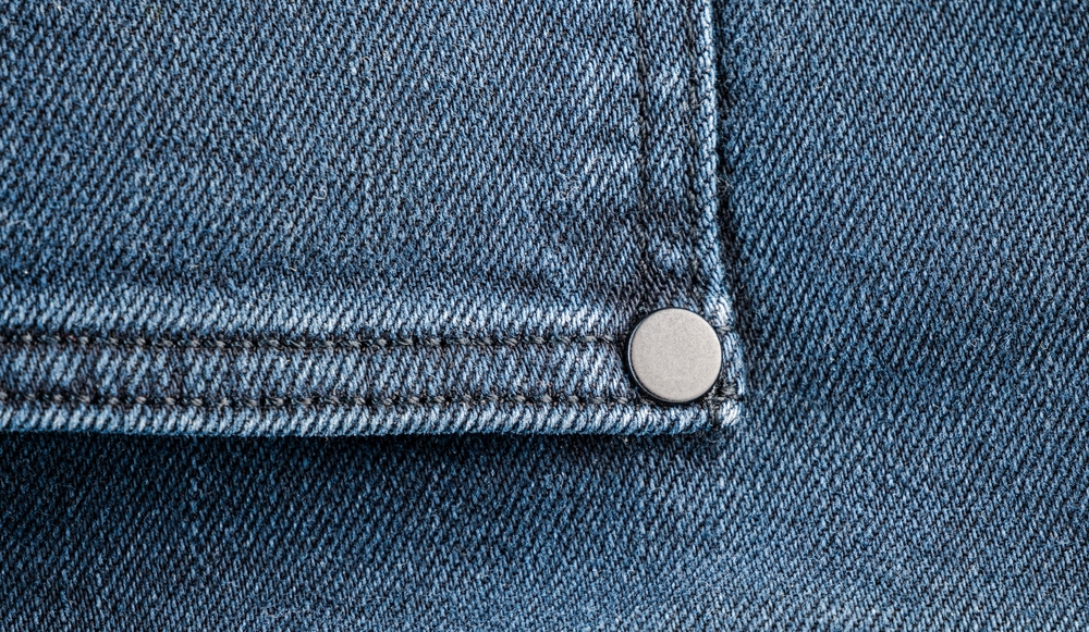 Close-up view of denim fabric with silver rivet detail