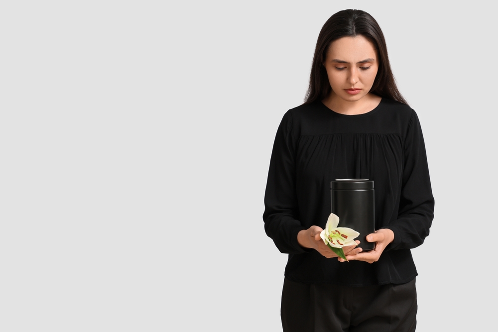 Young woman with mortuary urn and lily flower on white background