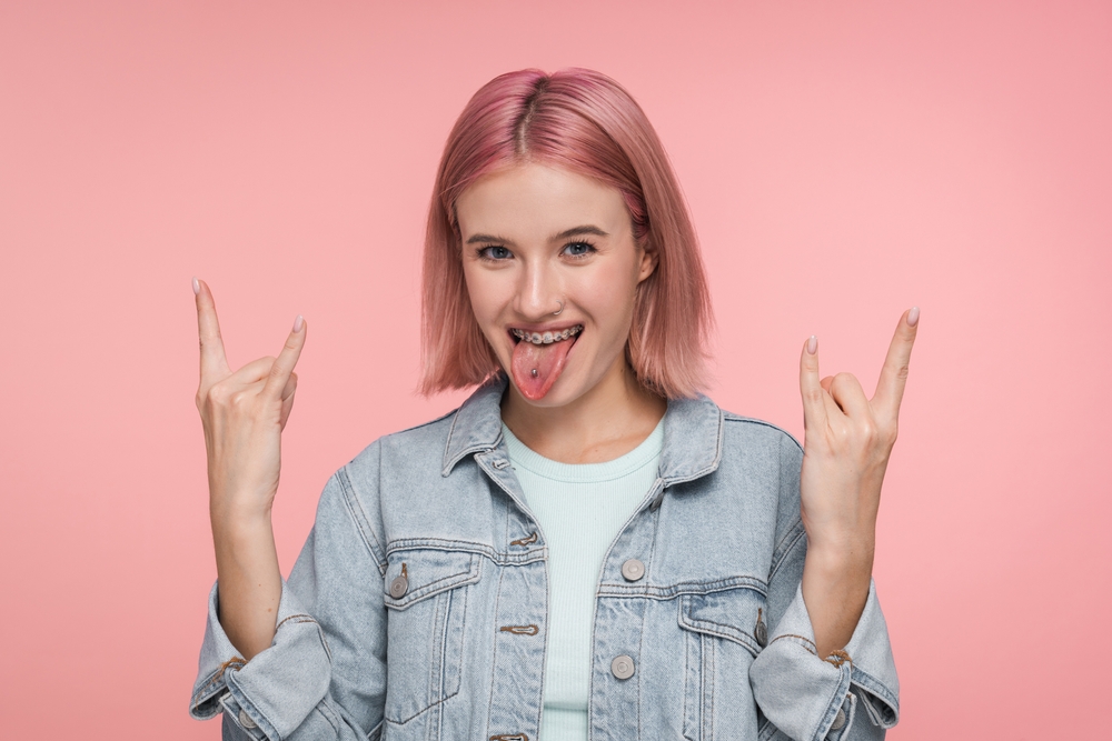 Enthusiastic excited crazy hipster woman girl female student with colorful hair piercing tongue having fun show rock-n-roll heavy metal sign screaming from joy and thrill isolated pink background