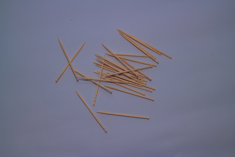 The image shows a pile of wooden toothpicks scattered. Some toothpicks are crossed, while others are placed randomly, featuring a grooved design at the ends.