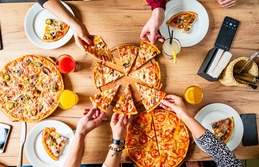 Friends joyfully share slices of pizza, surrounded by vibrant drinks and a warm atmosphere.