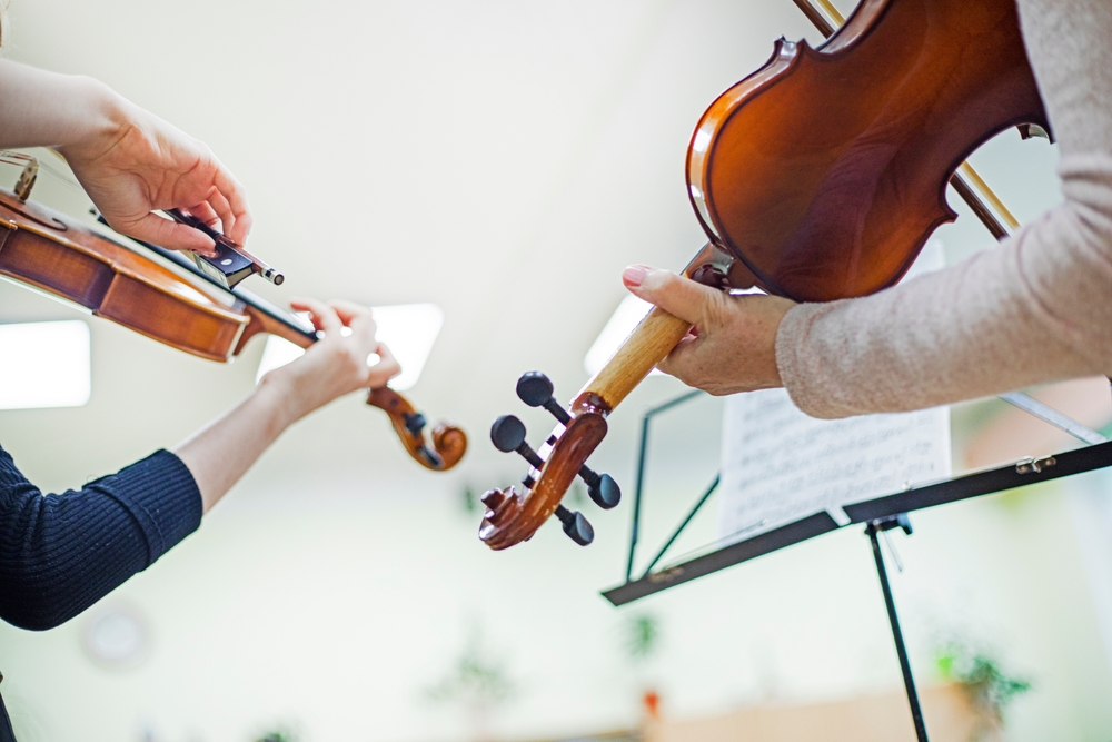 teenage violinist girl learning a piece from notes in a music class with a teacher. Musical development