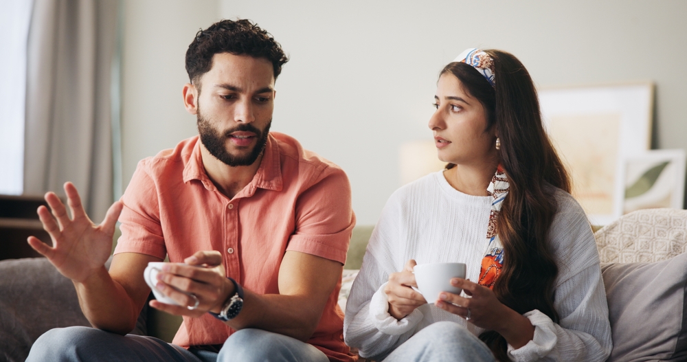 Couple, talk and coffee with fight on sofa for affair, cheating or stress with discussion in lounge. People, man and woman with conversation for dispute, argument and conflict with tea cup in home
