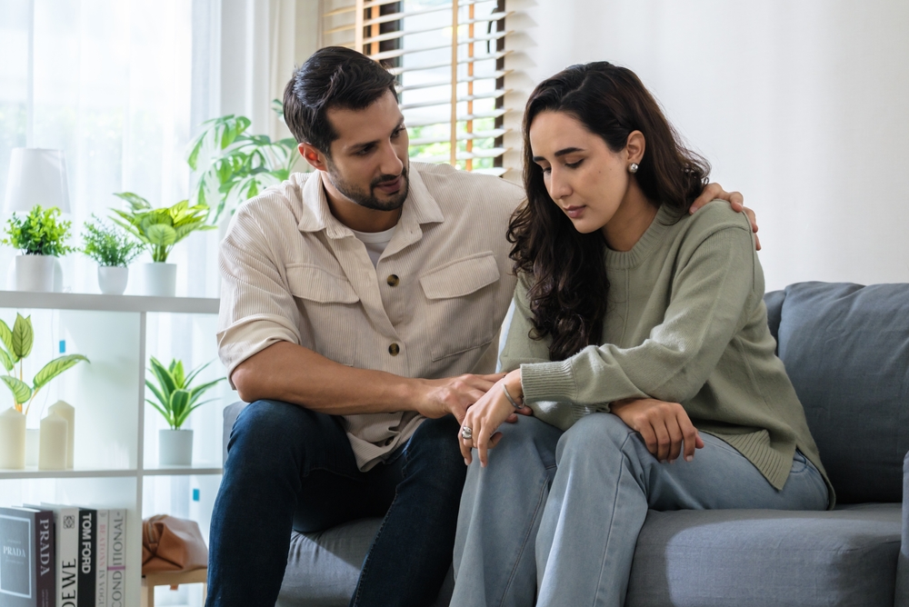 Supportive couple in emotional moment at home as woman struggles with sadness and stress, expressing