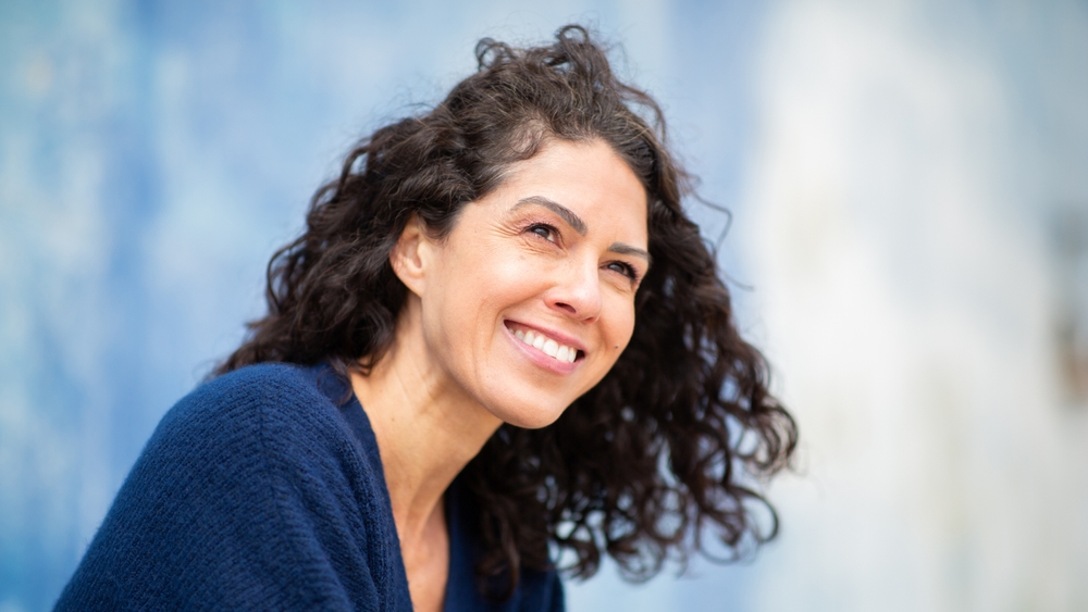 Close-up of a joyful woman with curly hair, smiling outdoors