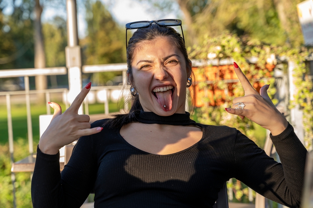 Young woman expressing rebellious attitude with a rock and roll hand sign and sticking out tongue