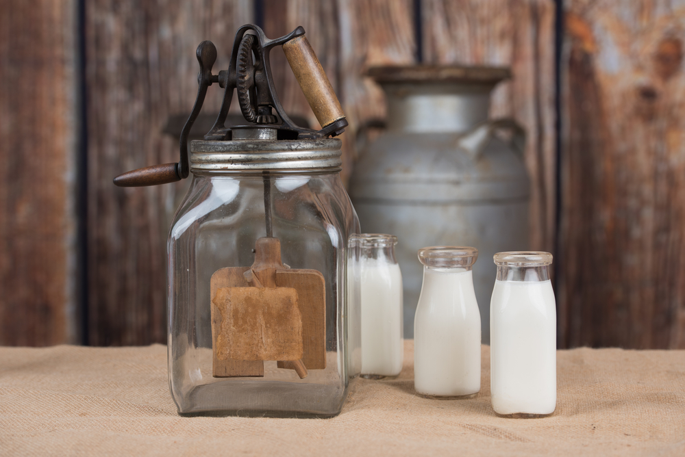 Butter churn with three dairy bottles and old milk cans in the background