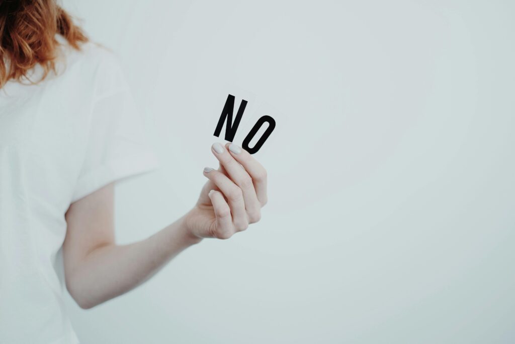 A woman in white with her hand only visible holding up the letters "NO" against a plain light background.