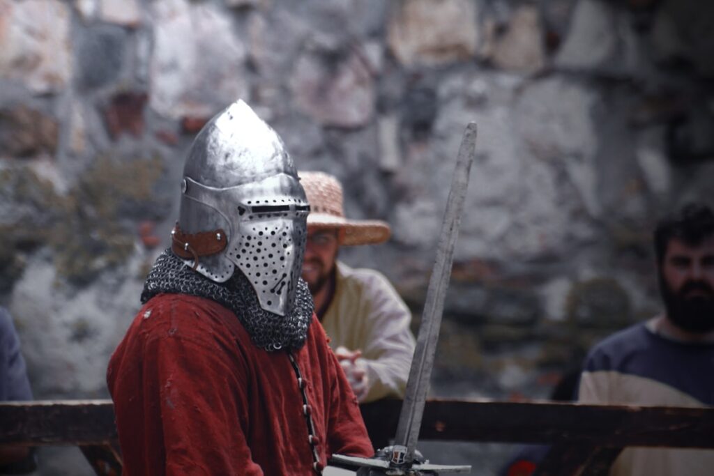 Medieval reenactor in chainmail, helmet, and red tunic holding a sword.