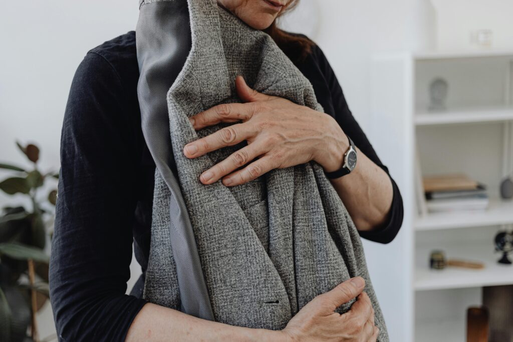 A person holding a gray jacket close to their chest.