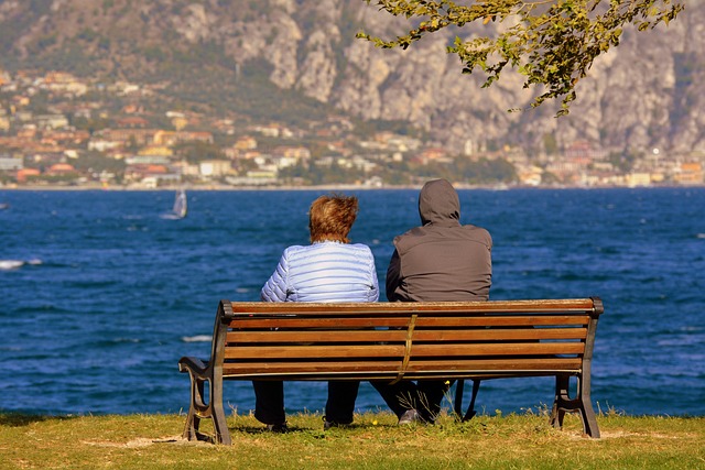 two senior citizens sitting on a bench by a lake.