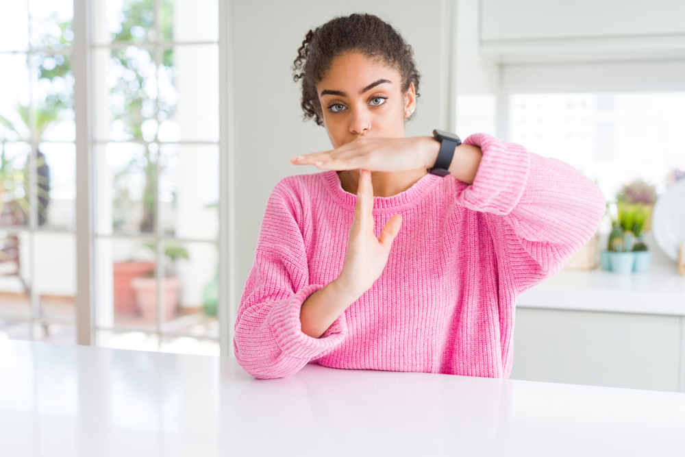 Beautiful african american woman with afro hair wearing casual pink sweater Doing time out gesture with hands, frustrated and serious face